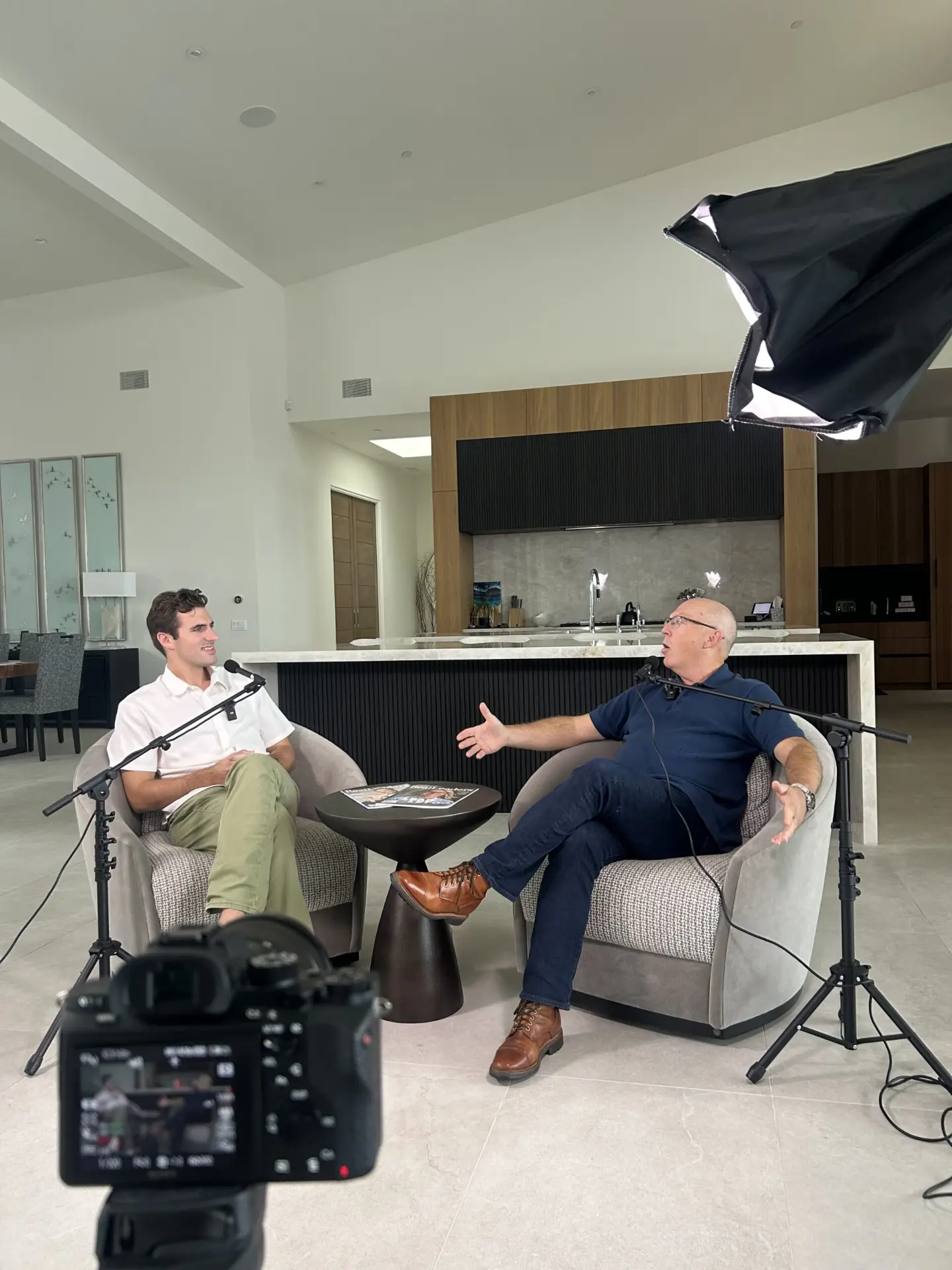 Two men seated in armchairs during a Real Leaders Studio interview, with cameras and lighting equipment in the foreground
